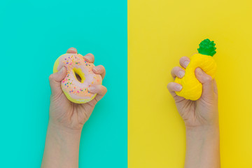 Flat lay antistress squish toys yellow pineapple,pink donut with sprinkles in hands.Bright blue background.Compressing,soft,squeezable items to relieve stress,problem,anxieties,worries.Summer concept