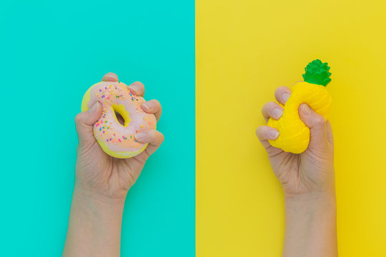 Flat lay antistress squish toys yellow pineapple,pink donut with sprinkles in hands.Bright blue background.Compressing,soft,squeezable items to relieve stress,problem,anxieties,worries.Summer concept