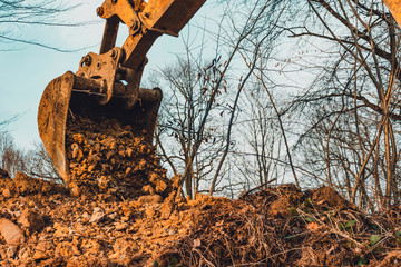 Backdrop of excavator bucket with soil on forest and sky background.