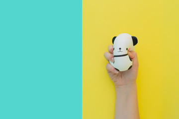 Flat lay antistress toy squish black white big panda squeezed in hand.Bright yellow blue...