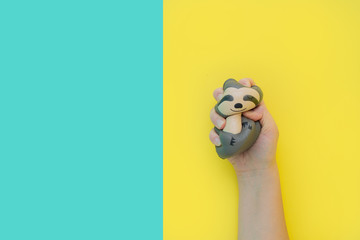 Flat lay antistress toy squish gray sloth squeezed in hand.Bright yellow blue...