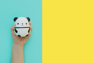 Obraz premium Flat lay antistress toy squish black white big panda squeezed in hand.Bright yellow blue background.Compressing, soft, squeezable items to relieve stress, problems, anxieties, worries.Summer concept
