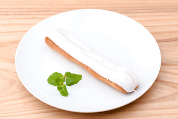 Traditional french dessert. Delicious eclair with custard and chocolate icing on a white plate with mint leaf.