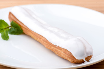 Traditional french dessert. Delicious eclair with custard and chocolate icing on a white plate with mint leaf.