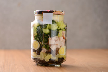 Homemade healthy russian salad Olivier with vegetables, meat and mayonnaise in glass jar on wooden table background