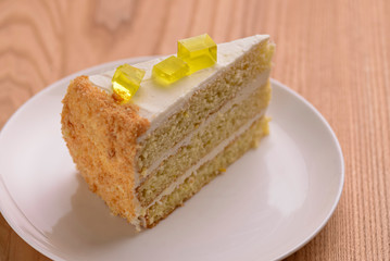 Lemon multi layered cake decorated with citron jelly and mint served on white plate on wooden background.