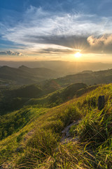 Fototapeta premium A beautiful scenery of sunset over Doi Pha Tang with a green grass field foreground in Chiang Rai, Thailand.