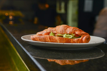Fresh baked croissant filled with ham and lettuce served on white plate in restaurant or cafe.