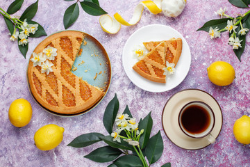 Delicious lemon pie slices with fresh lemons and a cup of tea on light background,top view