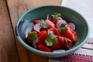 Healthy vegan lunch bowl. Ukrainian cuisine. Tomatoes with raw onions and parsley in a bowl on wooden table.
