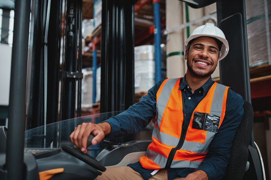 Young forklift driver sitting in vehicle in warehouse smiling looking at camera - Powered by Adobe