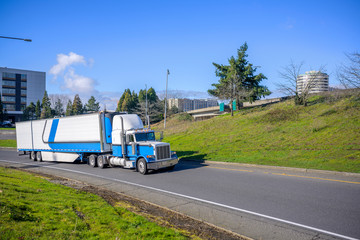 Classic bonnet American big rig semi truck transporting frozen cargo in refrigerator semi trailer running on highway exit road