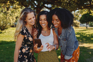 Portrait of a group of diverse young female friends watching something on smart phone in the park