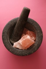 Pink Himalayan salt pieces set salt in a black granite mortar on a  pink background.Pink rock salt.Pink salt minerals in rock from Himalaya