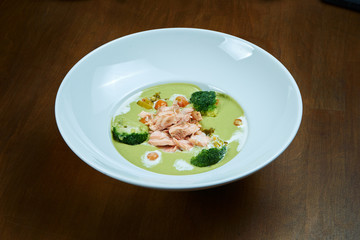 Appetizing and healthy green pea cream soup with broccoli and salmon cooked in a smoker on a wooden background. Close up