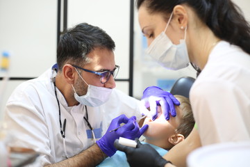 dentist is diagnosing the child while assistant in dental clinic