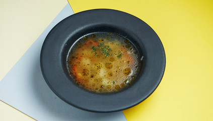 Dietary and healthy chicken stock with vegetables in a black bowl on a colored background. Close up view