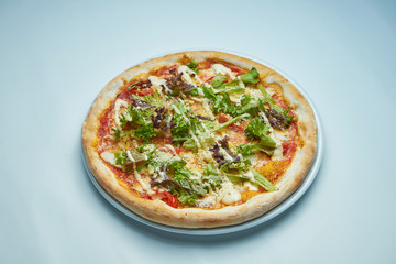 Appetizing baked Italian pizza with cream sauce, lettuce, chicken and parmesan on a white plate on a gray background. Pizza caesar
