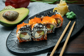Classic japanese sushi rolls with salmon, avocado, cream cheese and caviar. California roll on a black plate with chopsticks. Japanese cuisine. Healthy seafood