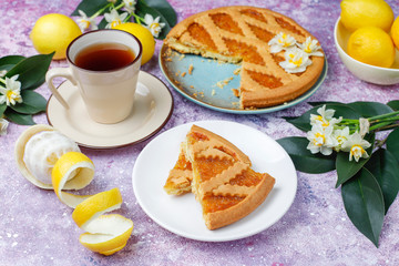 Delicious lemon pie slices with fresh lemons and a cup of tea on light background,top view