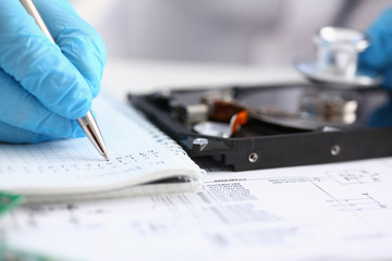 A male repairman wearing blue gloves holding stethoscope on hard drive from computer laptop in...