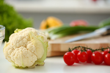 Cauliflower and cherry tomatoes lie on a cutting board in kitchen against backdrop of greenery healthy eating concept
