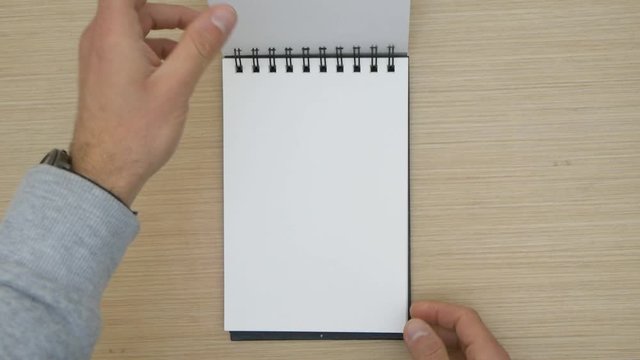 Man passing the sheets of a blank drawing pad. Blank spiral sketchpad.