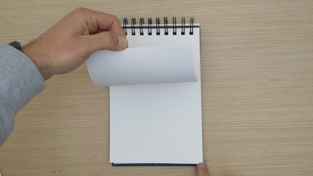Hands passing quickly sheets of a blank notepad on a wooden table. Art book sketch empty.