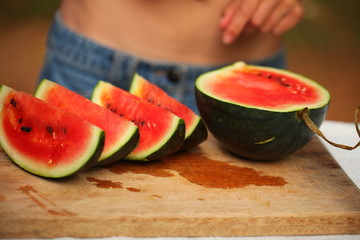 cutting fresh ripe watermelon into pieces with a knife on a wooden table