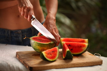 cutting fresh ripe watermelon into pieces with a knife on a wooden table