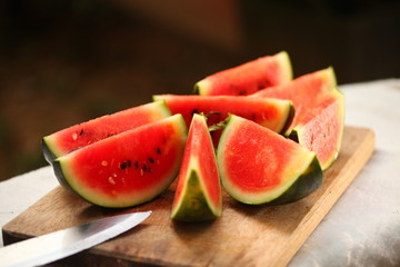 cutting fresh ripe watermelon into pieces with a knife on a wooden table