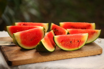 cutting fresh ripe watermelon into pieces with a knife on a wooden table