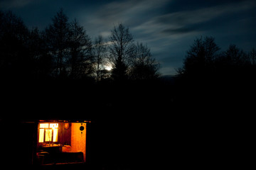 The window glows at night on a gloomy moonlit sky.