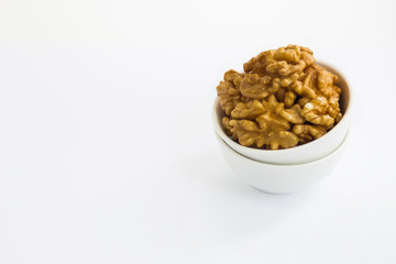 Peeled walnuts in white bowl on white background
