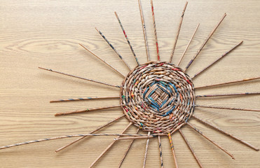 Hobbies and craft concept. Top view on weaving of the bottom of a basket of tubes twisted from newsprint on a wooden table. Flat lay, close-up, copy space