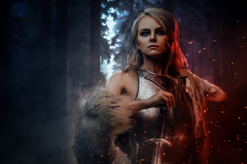 Beautiful warrior woman holding a sword wearing steel cuirass and fur in night forest. Fantasy...
