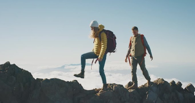 Young adventurous backpackers hiking to the top of a mountain above the clouds, happy couple hiking together in the great outdoors, amazing trekking on a mountain ridge