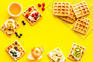 Breakfast with freashly baked belgian waffles on yellow background top-down frame copy space