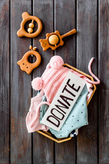 Charity concept. Donate text on box with clothes on dark wooden background top-down