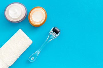 Cosmetology and skin care concept. Dermaroller, creams near flowers on blue background top-down copy space