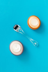 Dermaroller for mesotherapy near creams on blue background top-down flat lay