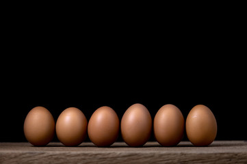 Chicken eggs are laid on a wooden table with a black background.