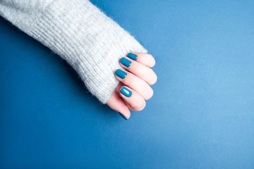 Beautiful female manicure on a blue background. Blue manicure on well-groomed hands