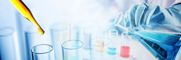 hand of scientist holding flask and pouring sample to test tube with dropping yellow liquid to test...
