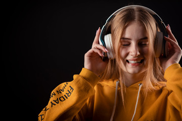 Young satisfied lady in yellow hoody touching headset enjoying music with closed eyes, isolated