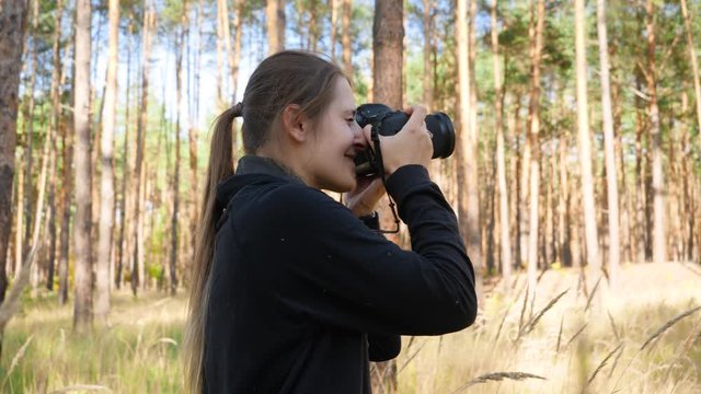 4k video of young female wildlife photographer making images of nature while standing in high grass at forest
