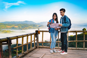 Asian tourist man and woman travel with map in forest. Beautiful Travelers Smiling Couple In Love have a good time in the mountains ,Holding camera In Hands While Traveling Together. Travel Concept