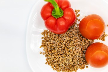 Fototapeta na wymiar Whole Bulgarian red pepper, two juicy fresh tomatoes and buckwheat in a white plate