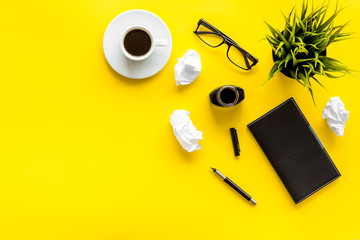 Journalist's desk. Notebook, pen, crumpled paper on yellow background top-down frame copy space