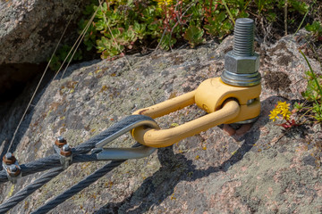 Anchor in rock holding a metall rope. Mounting metall rope to the rock.